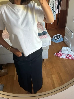 Svart långkjol i bomull - Stilren svart långkjol med rak passform och diskret slits framtill. Kjolen är tillverkad i bomull och har en klassisk look som är lätt att matcha med olika toppar. Etiketten är av så vet inte riktigt från vart, men har för mig H&M