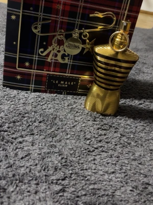 Jean Paul Gaultier Le Male Elixir - Säljer en Jean Paul Gaultier Le Male Elixir parfym i en snygg guldfärgad flaska formad som en manlig torso med horisontella ränder. Flaskan är i metall och har en unik, lyxig design. Perfekt för dig som gillar exklusiva dofter och coola flaskor.