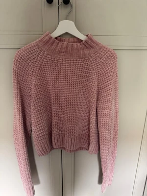 Rosa stickad tröja från H&M Divided - Mysig rosa stickad tröja från H&M Divided med grovstickad struktur och hög ribbad krage. Tröjan har långa ärmar och ribbade muddar vid ärmslut och nederkant. 
