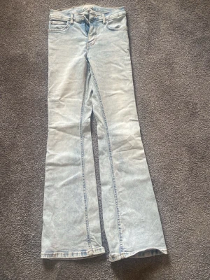 Ljusblå bootcut jeans - Säljer ett par ljusblå bootcut jeans med klassisk femficksmodell och hög midja. Jeansen har en snygg tvättad look och vida ben som ger en retrovibe. Perfekta för dig som gillar en avslappnad men trendig stil.