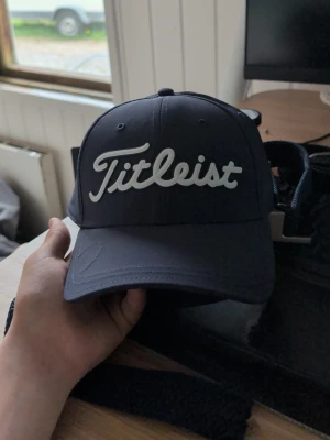 Mörkblå Titleist keps - Snygg mörkblå keps från Titleist med vit broderad logga framtill. Klassisk böjd skärm och justerbar rem baktill för perfekt passform. Perfekt accessoar för golfbanan eller vardagslooken.