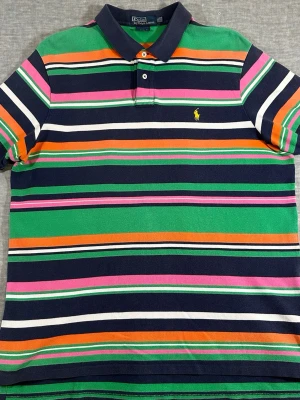 Vintage 2000’s Polo Ralph Lauren striped polo in a super clean colorful summer colorway 🌴XXL - Navy base with green, pink, orange and white stripes + yellow pony logo. Gives strong yacht club / coastal prep / resortwear vibe.  Custom Fit tagged XXL but fits relaxed and roomy perfect for summer. Thick quality cotton piqué fabric.  Condition is very good overall.  Measurements laid flat: P2P: 63 cm Shoulder to shoulder: 49 cm Length: 77 cm  Please compare measurements with a shirt you own for best fit ✌️