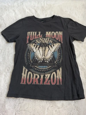 Svart t-shirt med tryck från Gina Tricot - Cool svart t-shirt från Gina Tricot med stort tryck framtill som har texten 'Full Moon Horizon Soul Search' och en fjäril. T-shirten har rund hals och korta ärmar. Perfekt för dig som gillar statement-plagg och snygga prints.