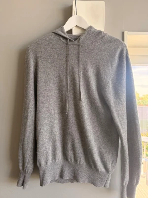 Soft goat hoddie  - Mjuk och stilren grå soft goat hoodie i kashmir med huva och snörning. Tröjan har ribbade muddar vid ärmslut och nederkant, perfekt för en chill och avslappnad look.