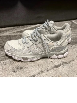 Gråa Asics sneakers med mesh och skinn - Snygga sneakers från Asics i ljusgrått med klassisk logga på sidan. Skorna har ovandel i mesh och detaljer i syntetiskt skinn, samt en vit och grå sula med cool design. Perfekta för en sportig och trendig look.