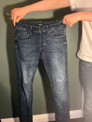 Mörkblå slim fit jeans från Jack and Jones  - Snygga mörkblå slim fit jeans från Nudie med klassisk femficksdesign och diskreta slitningar. Jeansen har normal midja, dragkedjegylf och är tillverkade i stretchig denim för en bekväm passform.