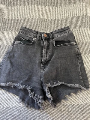 Gråa svarta högmidjade jeansshorts - Snygga grå svarta jeansshorts med hög midja och fransar. Helt perfekta för sommaren. Från hm i storlek 34.