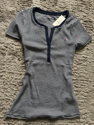 Hollister henley från 2000s vibes! - 💙 Cute Hollister henley från 2000s vibes! Marinblå/vit striped t-shirt med knappar framtill och broderad Hollister logo. Superstretchig och sitter så fint ✨ Perfekt basic till low rise jeans eller kjol. Strl: L men passar för mig som brukar ha S. Så tröjan är stretchig och kommer passa S-L💞 Skick: jättefint, med tags kvar 🤍 