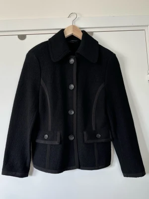 Marc O’Polo - svart jacka / kavaj, 100% ull - storlek 40 - Stilren svart jacka / kavaj från Marc O’Polo i storlek 40. Tidlös modell med klassisk krage och knappar framtill. Jackan har två fickor med lock och markerade sömmar längs sidorna för en snygg siluett. Väv-stickat tyg i 100% ull, så bra material som andas. En tidlös kvalitativt gjord klassiker som kommer hålla säsong efter säsong. Nypris 2800:-. Mycket gott skick, som ny! 