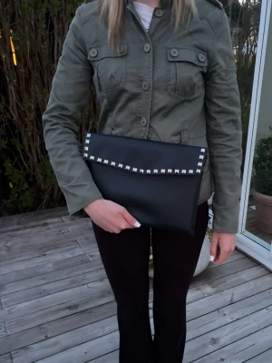 Datafodral med silvernitar - Stilrent datorfodral tillverkat av veganskt läder i vattentätt material. Fodralet stängs med knapp. Fodralet skyddar din dator effektivt samtidigt som det ger din outfit en extra touch. ⚜️ Storlek: 34 × 25 cm –  Innifrån 33 x 24 📦  