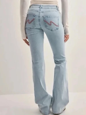 Ljusblå bootcut jeans med slitningar - Säljer ett par ljusblå bootcut jeans med slitna detaljer på knäna och broderade bakfickor. Jeansen har en klassisk femficksdesign och är perfekta för en avslappnad och trendig look.