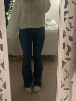 Blå bootcut jeans med broderade fickor - Säljer ett par klassiska blå bootcut jeans med snygga broderade bakfickor. Jeansen har normal/low waist midja, dom är lite slitna nere vid benen men inget som syns jätte mycket när dom sitter på, dom är från Nelly och passar både S och M