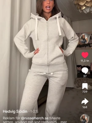 Ljusgrå hoodie från russemerch - Snygg ljusgrå hoodie från russemerch med dragkedja. Hoodien har huva med breda vita snören och ribbade muddar vid ärmslut och nederkant. Jätteskönt material och sparsamt använd. I storlek M.