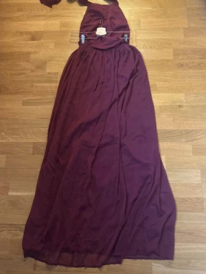 Vinröd långklänning med omlott - Säljer en vinröd långklänning med omlott och halterneck. Klänningen har ett elegant fall och knytband i nacken. Perfekt för speciella tillfällen när du vill känna dig extra fin.