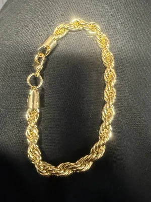 Tjockt guldfärgat rep-armband - Säljer ett snyggt armband i guldfärg med tvinnad repdesign. Armbandet har en rejäl karbinhake och glänser riktigt fint i ljuset. Perfekt för dig som vill ha en statement-accessoar som sticker ut.