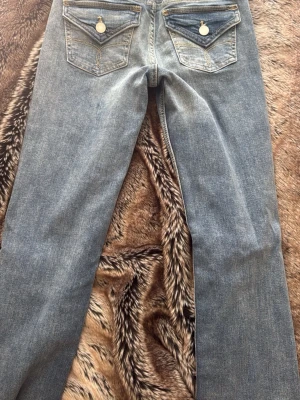 Blå bootcut jeans med fickdetaljer från bershka HELT NYA - Helt nya!! Säljer ett par blå bootcut jeans med snygg slitning och dekorativa fickor bak med knappdetaljer. Jeansen har klassisk femficksmodell och är tillverkade i denim. Perfekta för en avslappnad och trendig look.