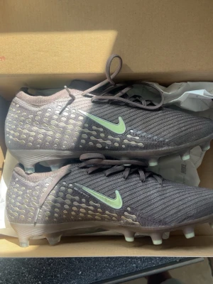 Nike vapor 16 mbappe fotbollsskor lila/gul - Säljer ett par Nike Zoom fotbollsskor i lila med gula detaljer och mönstrad ovandel. Skorna har fasta dobbar och är tillverkade i syntetmaterial för bra grepp och lätt vikt. Perfekta för dig som vill ha stilrena och funktionella skor på planen.