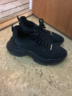 Svarta Steve Madden chunky sneakers med stickad ovandel - Snygga helsvarta sneakers med chunky sula och stickad ovandel. Skorna har rund tå, svarta skosnören och detaljer i metall framtill. Perfekta för en streetwear-look och riktigt bekväma tack vare den flexibla mesh-designen.