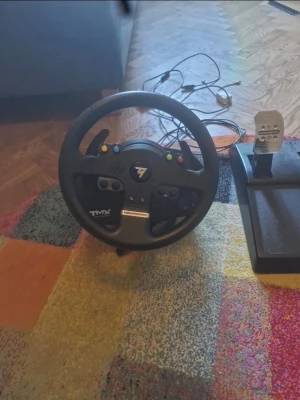 Thrustmaster TMX ratt och pedaler - Säljer ett Thrustmaster TMX racingset med ratt och pedalställ. Ratten är svart med flera knappar och har en rund form, medan pedalstället har tre metallpedaler på svart plastbas. Perfekt för racing- och bilspel på konsol eller PC. Skicket är mycket bra. Möjlighet att möta upp i Stockholm.