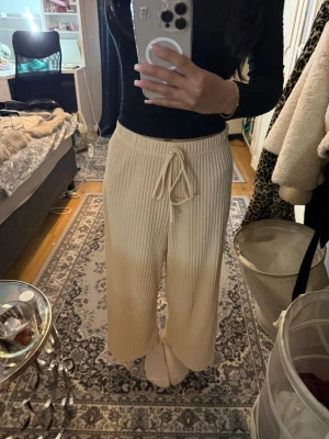 Beige linnebyxor - Säljer ett par beige linnebyxor med ribbad struktur och breda ben. Byxorna har justerbar dragsko i midjan för skön passform. Perfekta för chill dagar hemma eller när du vill vara bekväm men ändå se snygg ut. Materialet känns mjukt och stretchigt.