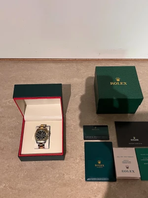 Role Daytona tvåtonad klocka - Snygg Role Daytona med svart urtavla och tvåtonad länk i silver och guld. Klockan har klassisk rund form, kronograf-funktion och levereras med originalbox och certifikat. Perfekt accessoar för dig som gillar exklusiv stil och detaljer.