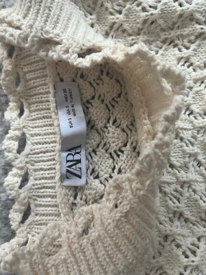 Vit virkad stickad tröja från Zara - Säljer en vit stickad tröja från Zara i storlek S. Tröjan har ett virkat, hålmönstrat material och ribbade kanter vid halsen. Perfekt för lager på lager och ger en trendig, bohemisk vibe till din outfit.