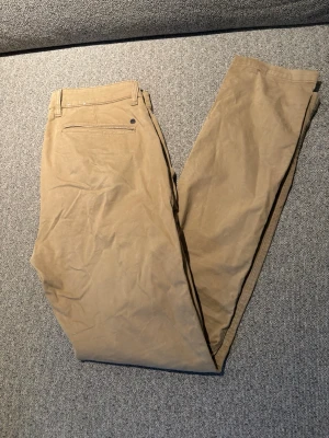 Beiga chinos från NN07 - Snygga beiga chinos från NN07 med klassisk rak passform och diskret bakficka med knapp. Perfekta för en stilren look och tillverkade i mjukt bomullstyg. Passar dig som gillar enkel och tidlös stil. Storlek W31 L32