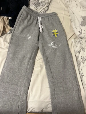 Gråa mjukisbyxor med Sverige-märke - Säljer ett par gråa mjukisbyxor med broderat Sverige-märke på vänster lår och vit, tjock dragsko i midjan. Byxorna har raka ben och är tillverkade i mjukt sweatshirtmaterial. Perfekta för chill dagar eller träning.byxor från gravitygrab med Sverige loggan har använt 2 gånger säljer billigt nypris 599