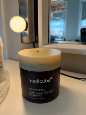 Medicube Deep Vita C Pad toner - Medicube Deep Vita C Pad är en toner i form av runda pads indränkta i vitaminvatten och vitamin C-derivat. Burken är brun med beige lock och innehåller pincett för enkel användning. Innehåller även niacinamid 2% för extra lyster och jämnare hudton.