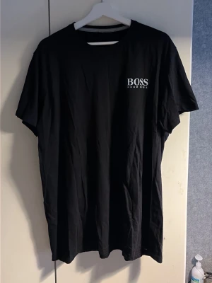Svart t-shirt från Hugo Boss - Snygg svart t-shirt från Hugo Boss med klassisk rund hals och diskret logga på bröstet. Enkel och stilren design som passar till det mesta. Tillverkad i mjuk bomull för skön känsla hela dagen.