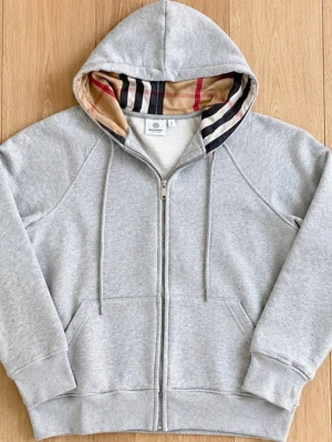 Grå zip hoodie med Burberry-mönster - Snygg grå zip hoodie från Burberry med klassiskt rutigt mönster i huvan. Tillverkad i mjuk bomullsblandning, har dragsko i huvan och två stora fickor framtill. Perfekt för en chill och stilren look.