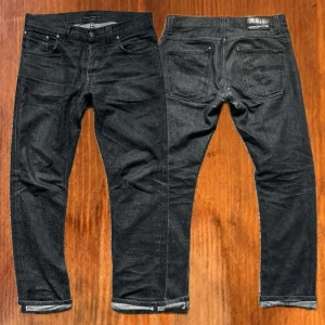 Selvage nudie jeans - Nudie jeans grim Tim dry black selvage i storlek 32/32. Jeansen har lagats på en del ställen som man kan se på bilderna, men det är inget som syns när man har dem på sig. Hör av er om ni har några andra funderingar!