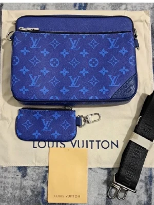 Blå axelväska Louis Vuitton monogram - Säljer en blå axelväska från Louis Vuitton med klassiskt monogrammönster i olika blå nyanser. Väskan har en avtagbar axelrem, en mindre matchande pouch och silverfärgade metalldetaljer. Perfekt för dig som vill ha en statementväska med lyxig känsla.