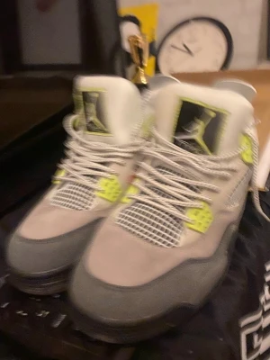 Nike Air Jordan 4 Neon sneakers - Snygga Air Jordan 4 sneakers i grå mocka med detaljer i neon och svart. Skorna har vita meshpaneler, vita och grå skosnören samt den klassiska Jumpman-loggan på plösen. Perfekt för dig som vill sticka ut med en unik färgkombination.