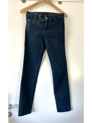 Stella McCartney - Mörkblå jeans - storlek S - Stilrena blå/ mörkblå jeans från Stella McCartney i storlek S. Klassisk femficksmodell med hällor för bälte och stängs med knapp och dragkedja. Knapparna är präglade med Stella McCartney-logotypen. En diskret logotyp finns även på en läderpatch baktill i midjan. Elastisk denim för bästa passform. Fint skick!