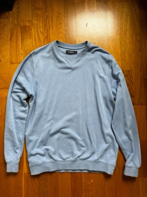 Ljusblå sweatshirt från Dressmann - En stilren ljusblå sweatshirt från Dressmann med rund halsringning och ribbade muddar vid ärmslut och nederkant. Tröjan har en relaxed fit och är tillverkad i mjukt bomullsmaterial. Perfekt för en chill och enkel look.