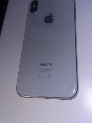 Silver iPhone X med glasbaksida - Säljer en stilren silverfärgad iPhone X från Apple. Telefonen har en snygg glasbaksida, rundade hörn och dubbla kameror på baksidan. Klassisk Apple-design med metallram och stor skärm på framsidan. Perfekt för dig som gillar modern teknik och enkel design.