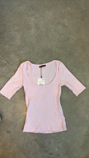 Ljusrosa topp från ZARA - Supersöt ljusrosa topp från ZARA med djup rundringning och tre kvarts ärmad. Helt ny och oanvänd, skriv om du har några funderingar