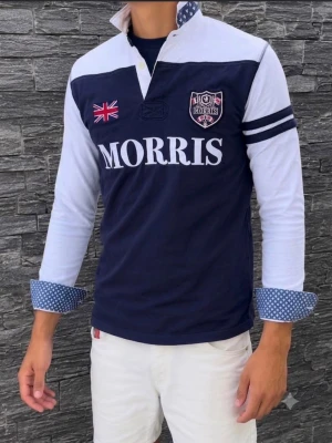 (Intressekoll)Blåvit henley från Morris - Snygg långärmad henley från Morris i marinblått och vitt med tryckt logga, brittisk flagga och emblem på bröstet. Skjortan har kontrasterande prickigt tyg i krage och manschetter samt två mörkblå ränder på ena ärmen.