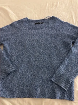 Blåmelerad stickad tröja - Mysig blåmelerad stickad tröja med rund halsringning och långa ärmar. Tröjan har ribbade muddar vid ärmslut och nederkant, vilket ger en skön och avslappnad passform. Perfekt för kyliga dagar och enkel att matcha med jeans eller kjol.