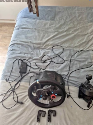Logitech ratt, pedaler och växelspak - Säljer ett komplett racing set från Logitech med ratt, pedaler och separat växelspak. Ratten är svart med detaljer i metall och har flera knappar samt en röd vridknapp. Pedalerna är i metall och plast, och växelspaken är svart. Perfekt för racing på konsol eller PC.