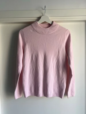 Ljusrosa stickad polotröja från Cashemere Feeling - Mysig ljusrosa stickad tröja med hög krage och långa ärmar från Cashmere Feeling. Storlek S men passar mer som XS. Liknar Gina tricot och Vera Moda. Tröjan har en enkel och stilren design med ribbstickad kant vid hals, ärmslut och nederkant. Material är akryl. Perfekt för kalla dagar och lätt att matcha med olika outfits.