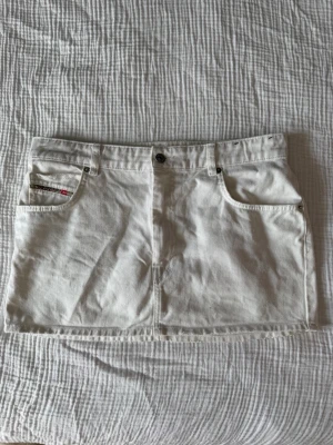 Vit jeanskjol med fickor - Säljer en vit kort jeanskjol med klassiska fickor fram och bälteshällor. Kjolen har knapp och dragkedja framtill och är perfekt för en trendig och avslappnad look. Passar till det mesta och är enkel att styla. Står storlek 32 på lapp midja 32 antar jag att de menar 