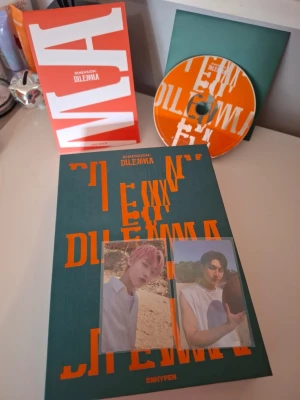 ENHYPEN Dimension: Dilemma album - Säljer ENHYPENs album 'Dimension: Dilemma' som innehåller fotobok, CD, två photocard och en poster. Albumet har en grön och orange design med tydlig text och coolt grafiskt tryck. Perfekt för dig som samlar på K-pop eller gillar ENHYPEN.