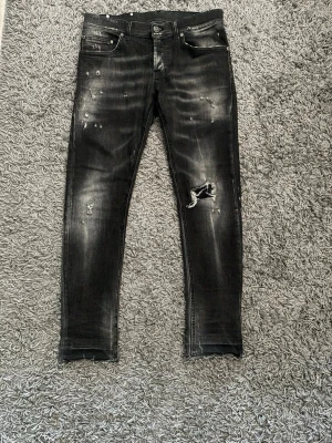 Dondup - 39cm bredd 90cm längd. Säljer ett par svarta skinny jeans med slitningar och hål på ena knät. Jeansen har en tvättad look med ljusare partier och detaljerade slitningar framtill. Klassisk femficksmodell och smal passform. Perfekta för en edgy streetstil.