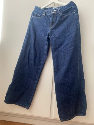 Mörkblåa wide leg jeans - Snygga mörkblå jeans med wide leg-modell och klassisk femficksdesign. Jeansen har låg/medel midja och raka, vida ben som ger en avslappnad och trendig look. Tillverkade i klassisk denim med synliga sömmar.