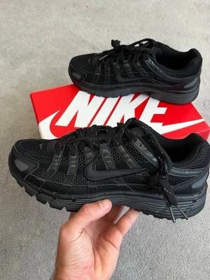 Nike svarta sneakers mesh och skinn - Säljer ett par helsvarta Nike sneakers med cool design i mesh och syntetläder. Skorna har låga skaft, robust sula och klassisk Nike Swoosh på sidan. Perfekta för dig som gillar sportig och stilren look.