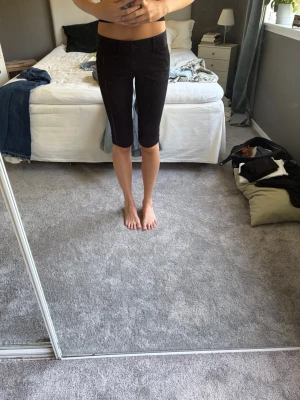 Svarta knälånga Capris  - Säljer ett par svarta, knälånga capris med tight passform och midwaist. Shortsen är i stretchigt material och passar perfekt till sommaren. Klassisk design utan synliga detaljer som knappar eller dragkedja.