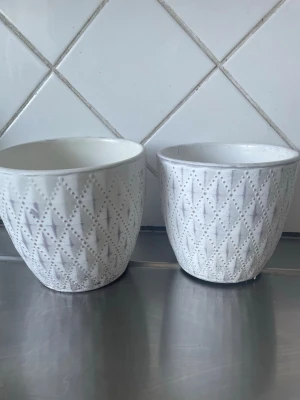 Två vita krukor med mönster - Säljer två vita krukor i keramik med upphöjt diamantmönster. Perfekta för växter eller dekoration. Stilrena och passar bra i moderna hem. Säljes tillsammans.