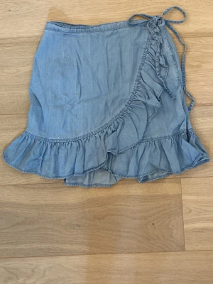 Ljusblå omlottkjol med volang från Asos - Söt ljusblå kortkjol i omlottmodell med volangkant och knytband i midjan i storleken S/36. Kjolen har en avslappnad, feminin look som passar perfekt till sommaren. Den är lite skrynklig nu, men fråga om du vill att jag stryker den innan jag skickar! Bara använt en enstaka gång💕60 kr + frakt